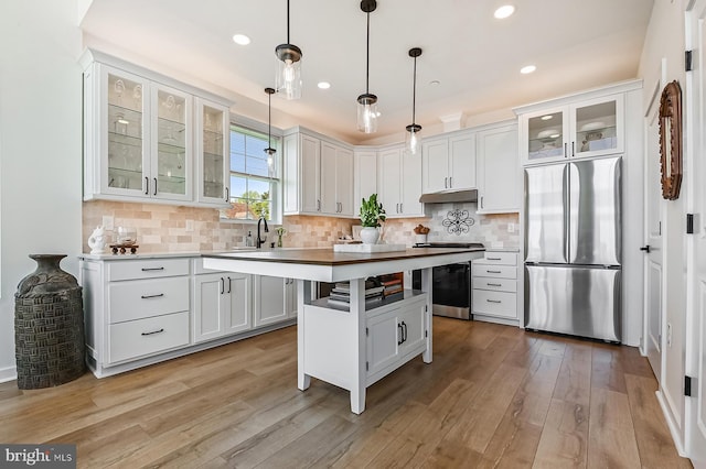 kitchen featuring stainless steel appliances, under cabinet range hood, light wood finished floors, glass insert cabinets, and tasteful backsplash