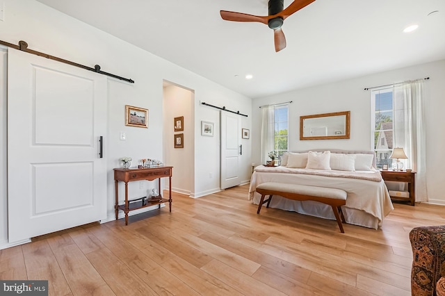 bedroom with a barn door, light wood finished floors, recessed lighting, baseboards, and ceiling fan