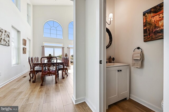 bathroom featuring wood finished floors, baseboards, a towering ceiling, vanity, and toilet