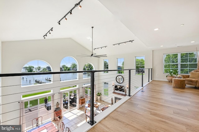 corridor with rail lighting, light wood finished floors, vaulted ceiling, recessed lighting, and baseboards