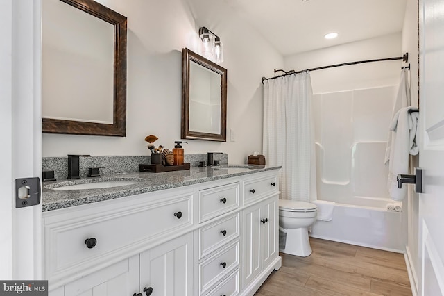 bathroom featuring toilet, wood finished floors, double vanity, and shower / tub combo