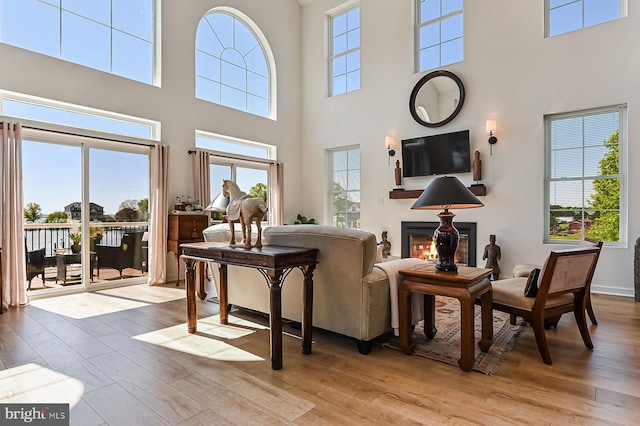 living area with a high ceiling, wood-type flooring, and a glass covered fireplace