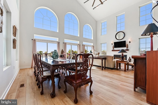 dining area featuring high vaulted ceiling, light wood-style floors, and baseboards