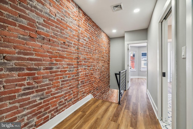 corridor with brick wall, baseboards, wood finished floors, and recessed lighting