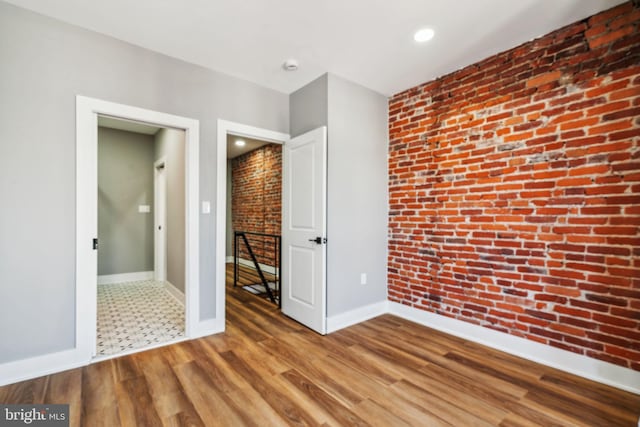 unfurnished bedroom featuring baseboards, brick wall, wood finished floors, and recessed lighting