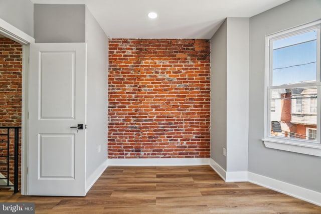 unfurnished room featuring baseboards, wood finished floors, recessed lighting, and brick wall