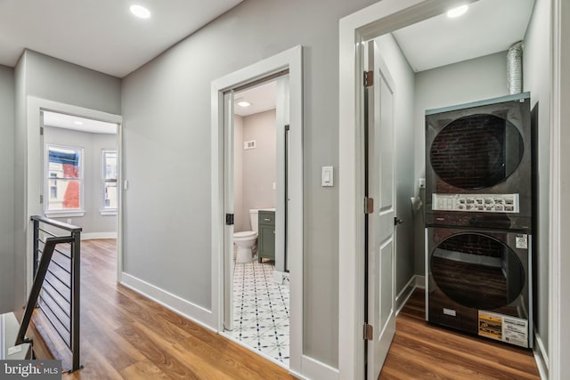 corridor with stacked washing machine and dryer, an upstairs landing, wood finished floors, baseboards, and recessed lighting