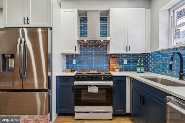kitchen featuring appliances with stainless steel finishes, wall chimney range hood, a sink, white cabinetry, and backsplash