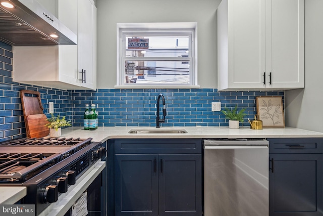kitchen with appliances with stainless steel finishes, ventilation hood, a sink, light countertops, and white cabinets
