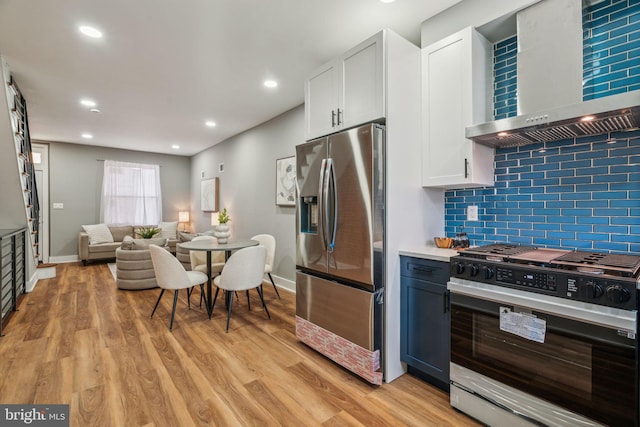 kitchen featuring stainless steel fridge, range with gas cooktop, wall chimney range hood, open floor plan, and decorative backsplash