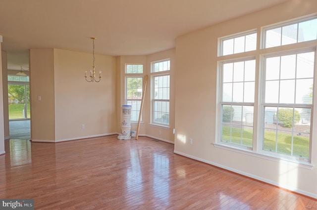 empty room featuring wood-type flooring, baseboards, and a chandelier
