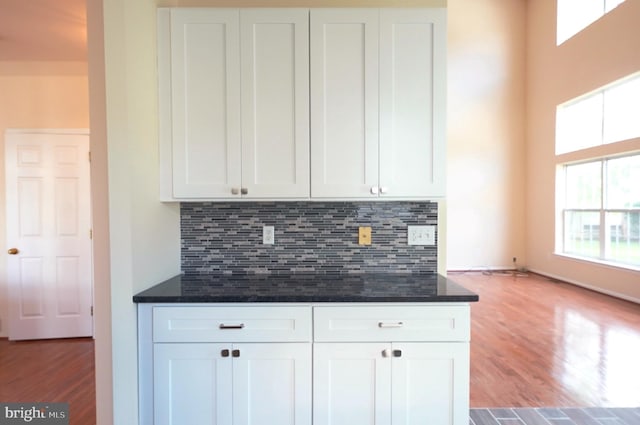 kitchen with white cabinets, wood finished floors, backsplash, and dark stone counters