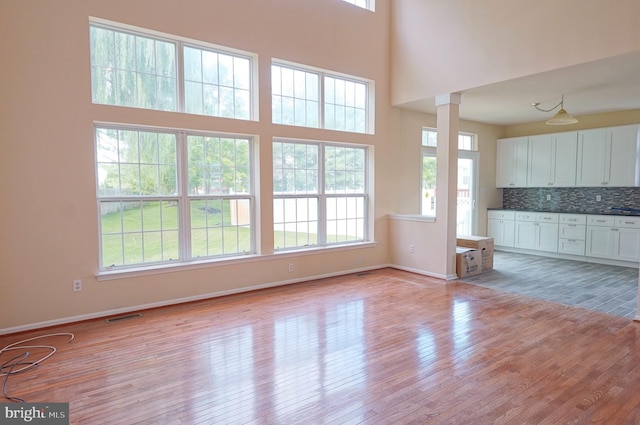 unfurnished living room with light wood-style floors, baseboards, a towering ceiling, and decorative columns