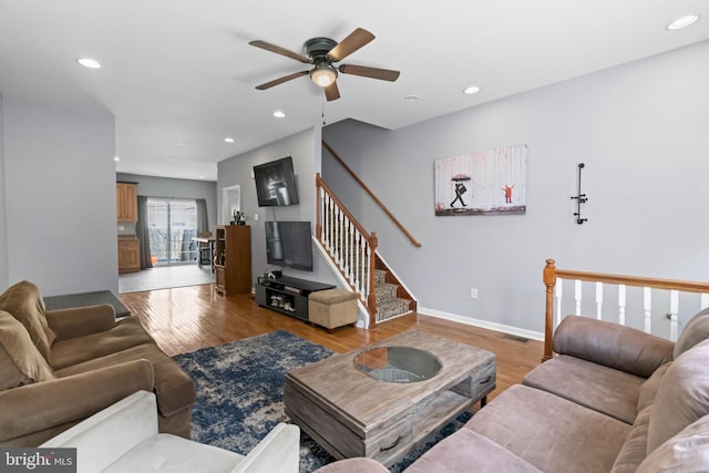 living room featuring a ceiling fan, light wood finished floors, baseboards, recessed lighting, and stairs