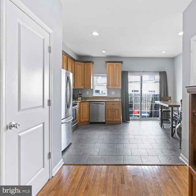 kitchen with appliances with stainless steel finishes, hardwood / wood-style flooring, recessed lighting, light countertops, and a sink
