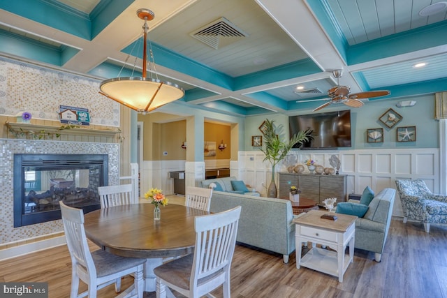 20785 Rodney Dr, Rehoboth Beach, DE 19971 - dining space with coffered ceiling, a tiled fireplace, a decorative wall, wood finished floors, and a ceiling fan