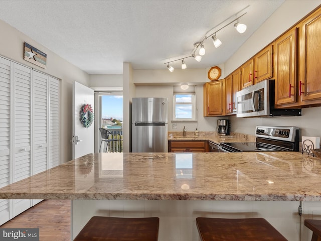 117 76th St Unit 302, Ocean City, MD 21842 - kitchen featuring appliances with stainless steel finishes, a peninsula, light stone countertops, a textured ceiling, and brown cabinetry