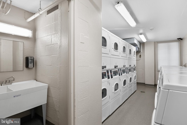 communal laundry room with estacked washer and dryer, washing machine and dryer, and concrete block wall