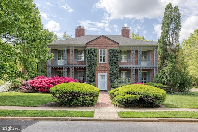 colonial inspired home featuring brick siding, a balcony, a front yard, and a chimney
