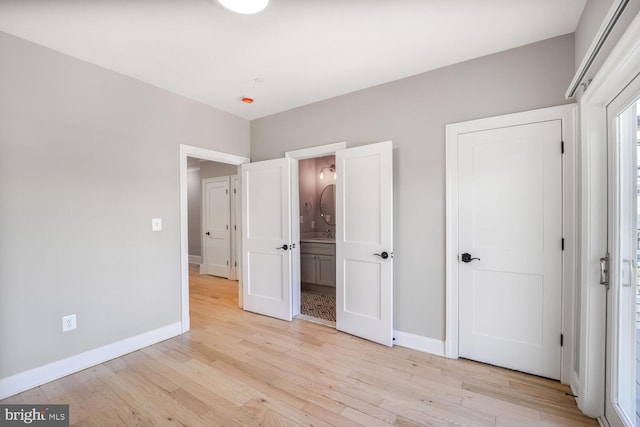 unfurnished bedroom featuring baseboards, light wood-type flooring, and ensuite bathroom