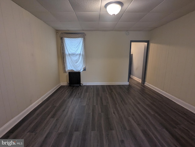 4133 Eierman Ave, Baltimore, MD 21206 - unfurnished room featuring radiator, a drop ceiling, dark wood-style flooring, wooden walls, and baseboards