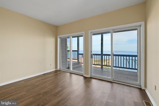 unfurnished room with dark wood-style floors, a water view, and baseboards