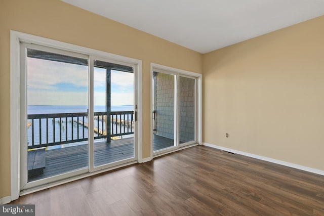 spare room with wood finished floors, a water view, and baseboards