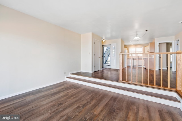 unfurnished living room with wood finished floors, baseboards, and stairs
