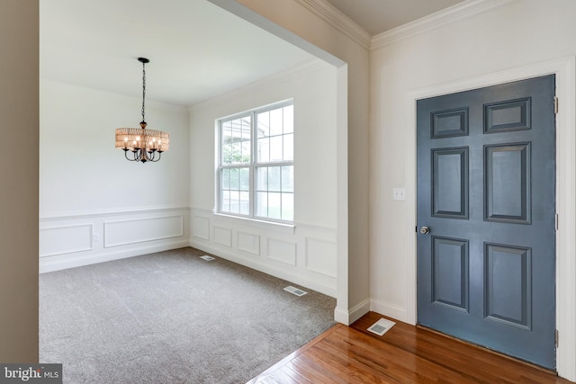 foyer entrance featuring crown molding, a chandelier, a wainscoted wall, and wood finished floors