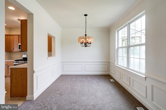 unfurnished dining area featuring a chandelier, wainscoting, crown molding, a decorative wall, and light carpet