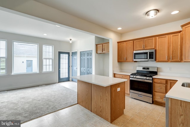 kitchen featuring appliances with stainless steel finishes, light carpet, a kitchen island, light countertops, and brown cabinets