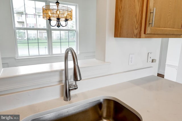 kitchen view of a sink, a chandelier, brown cabinetry, light countertops, and decorative light fixtures