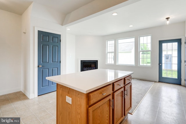 kitchen featuring baseboards, a glass covered fireplace, a center island, recessed lighting, and light countertops