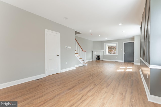 unfurnished living room featuring light wood-type flooring, stairway, baseboards, and recessed lighting