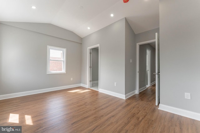 spare room featuring wood finished floors, lofted ceiling, baseboards, and recessed lighting