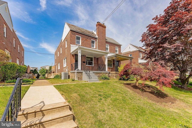 view of front of home with brick siding, covered porch, a front yard, a chimney, and central air condition unit