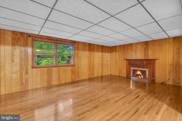 unfurnished living room featuring wood finished floors, a brick fireplace, wood walls, and a drop ceiling