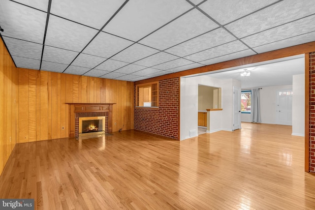 unfurnished living room featuring a fireplace, wood finished floors, wooden walls, and a drop ceiling