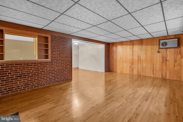 unfurnished room featuring wood finished floors, wooden walls, and a drop ceiling