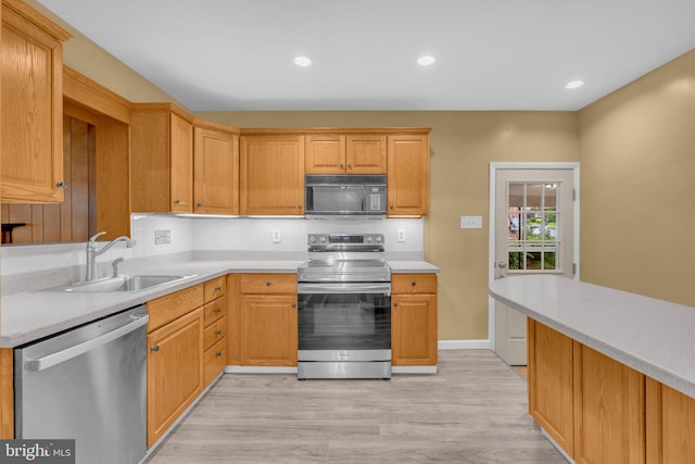 kitchen with stainless steel appliances, a sink, light countertops, light wood-type flooring, and decorative backsplash