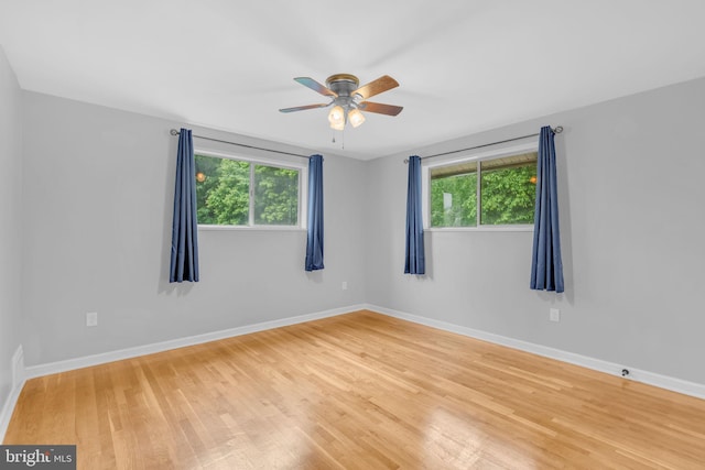 unfurnished room with plenty of natural light, wood finished floors, a ceiling fan, and baseboards