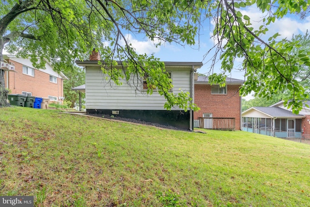 back of house featuring a sunroom, a yard, a chimney, and brick siding