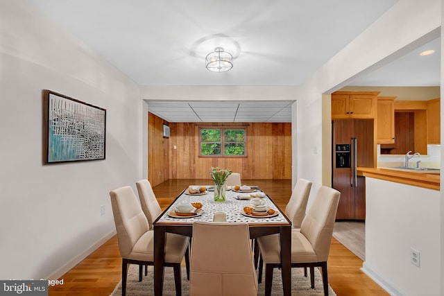 dining space featuring light wood-style flooring, baseboards, and wooden walls
