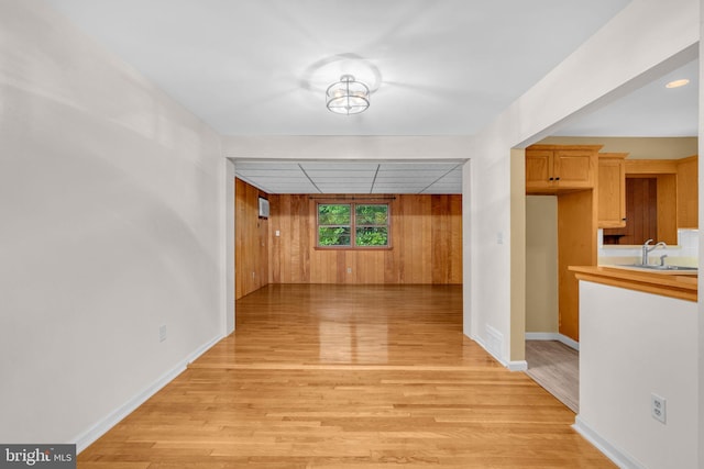 corridor with a sink, light wood-type flooring, baseboards, and wooden walls