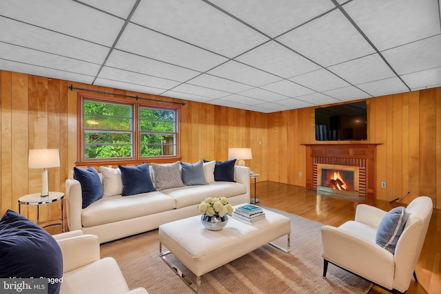 living room featuring wooden walls, wood finished floors, and a brick fireplace