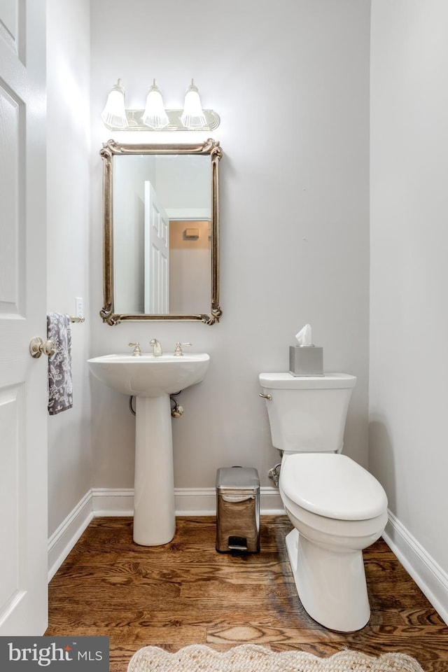 half bath featuring baseboards, wood finished floors, and toilet