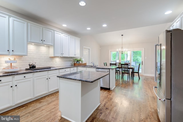 kitchen with appliances with stainless steel finishes, a peninsula, white cabinets, backsplash, and light wood-style flooring