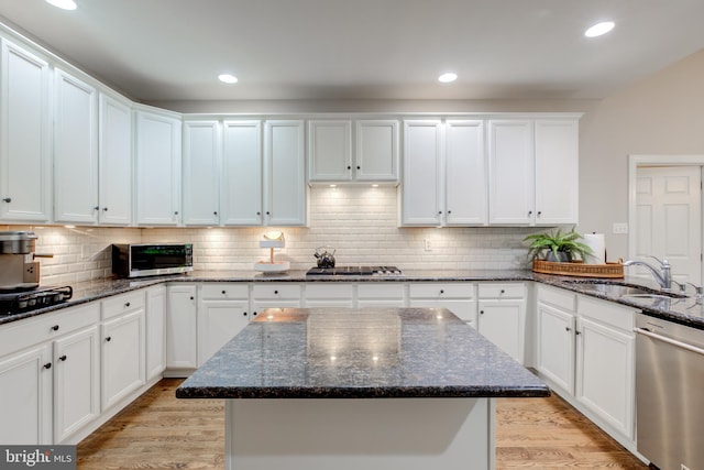 kitchen with stainless steel appliances, a sink, white cabinets, light wood-type flooring, and tasteful backsplash