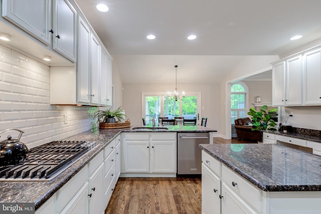 kitchen with appliances with stainless steel finishes, a sink, lofted ceiling, white cabinetry, and wood finished floors