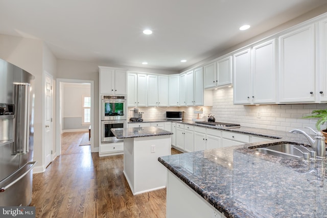 kitchen featuring stainless steel appliances, a sink, dark stone counters, wood finished floors, and white cabinetry